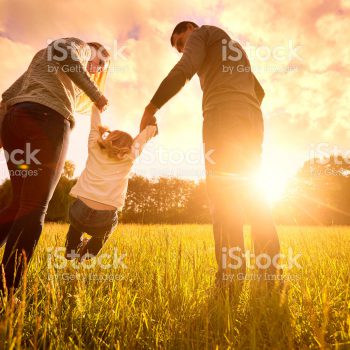 Happy family in the park evening light. The lights of a sun. Mom, dad and baby happy walk at sunset. The concept of a happy family.Parents hold the baby's hands.